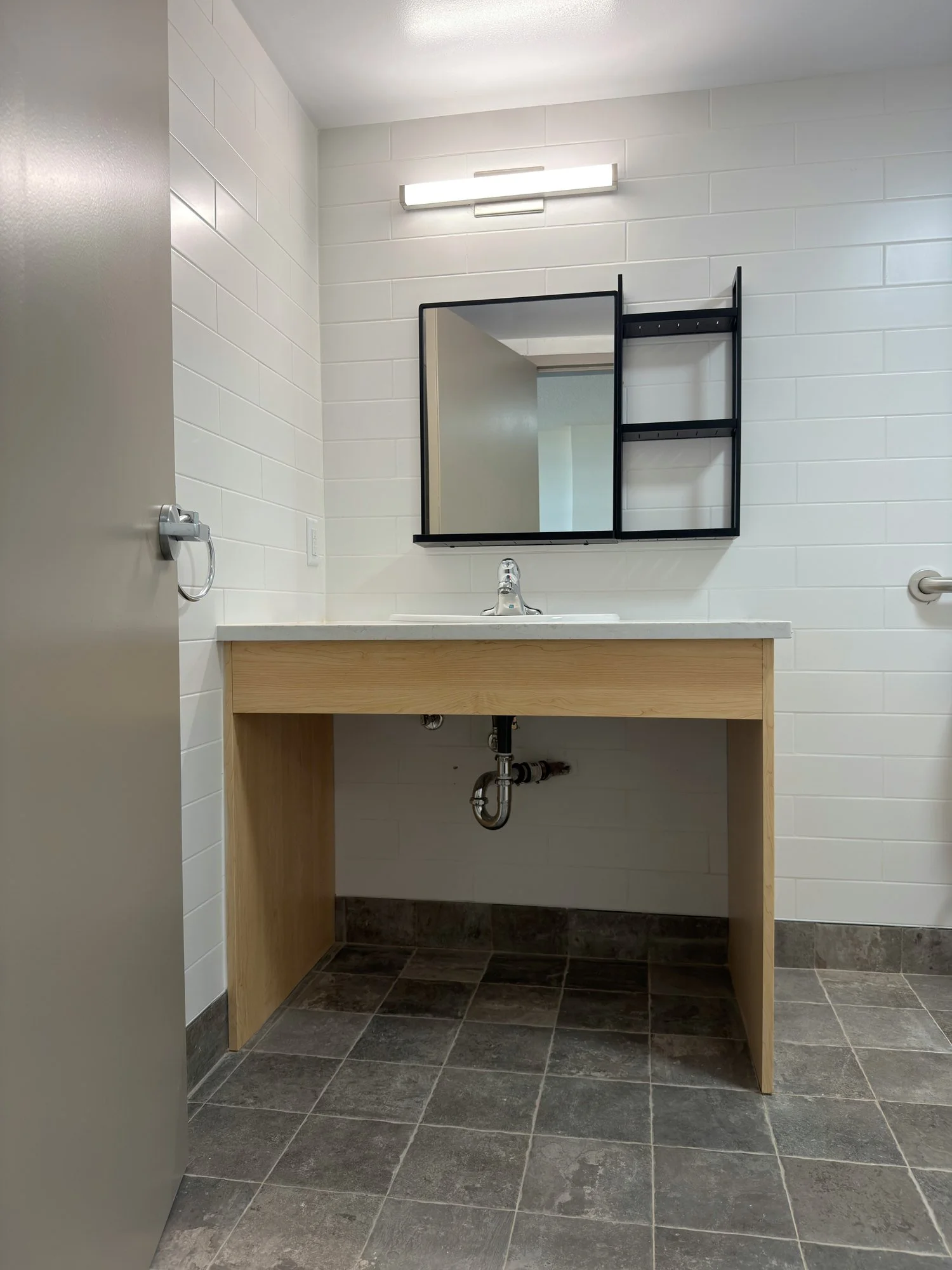 Light wood-look vanity with open knee space under the sink and a mirror with shelf above