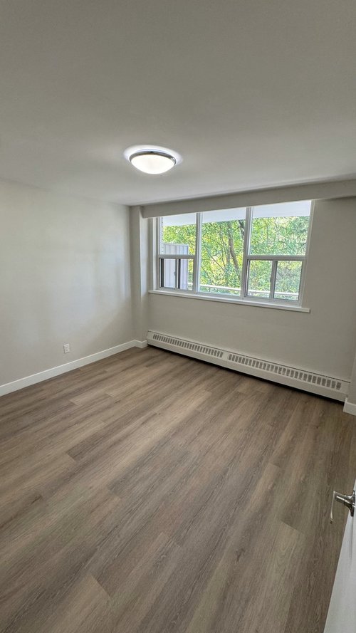 Finished bedroom with freshly painted light walls, white baseboards, a window and a new wood-look plank floor