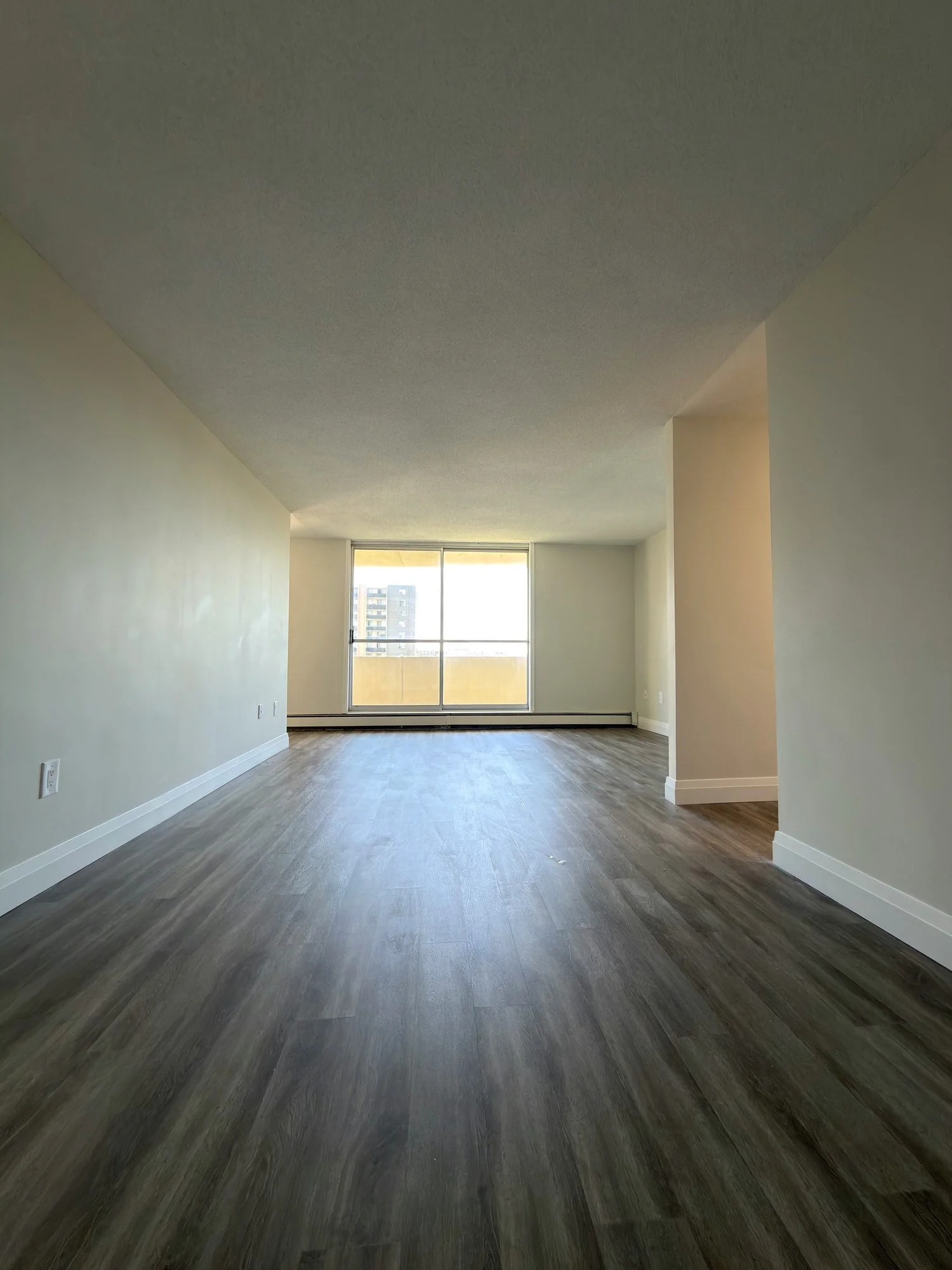 Long empty living room with wood-look plank floor and large windows at the far end