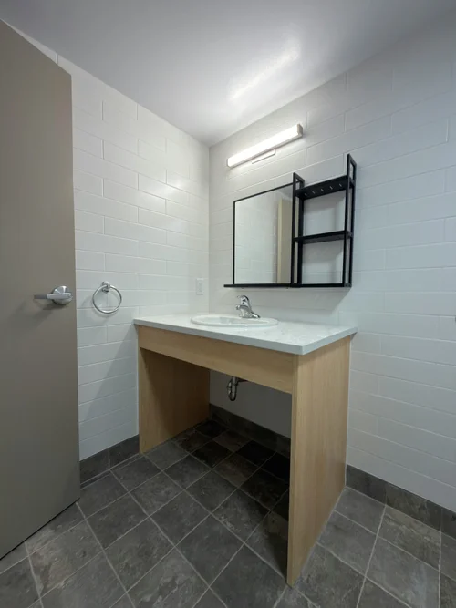 Roll-under vanity with light counter, wood-look base, mirror with shelf and white tile wall