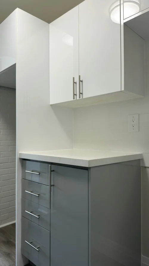 Kitchen corner with white upper cabinets and grey drawers under a light counter