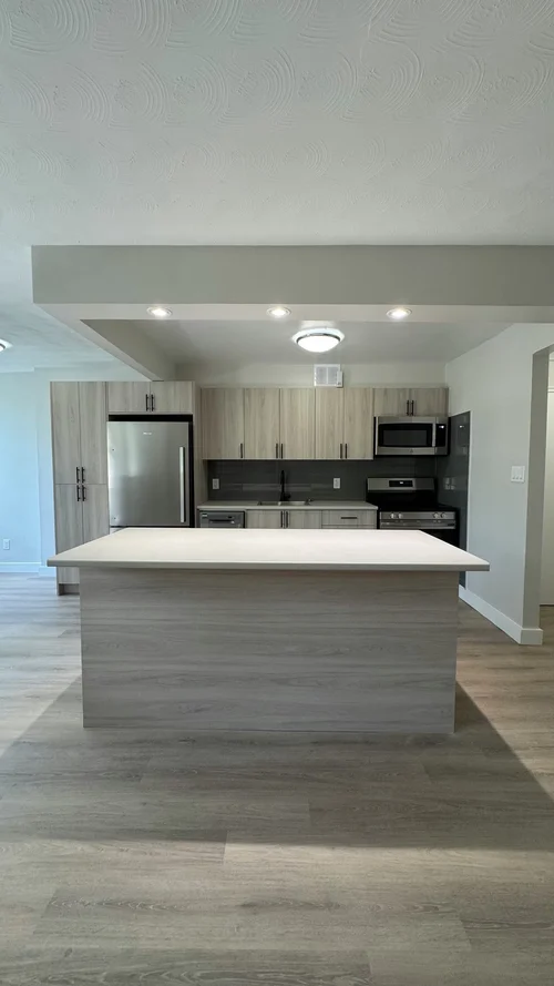 Open kitchen with light island and stainless appliances on wood-look floor
