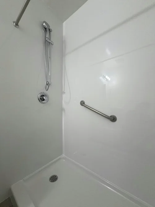 White shower with a drain, hand shower on a rail, control valve and a stainless grab bar