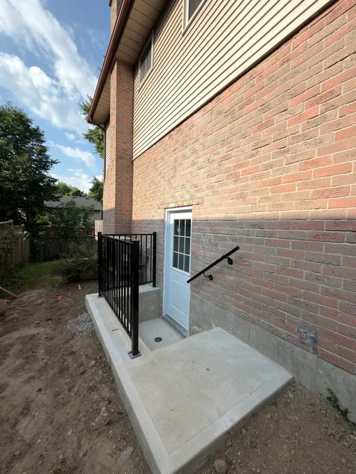 Walkout basement door with black metal railing on a new concrete landing