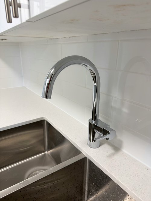 Chrome gooseneck faucet beside a stainless steel sink and white counter