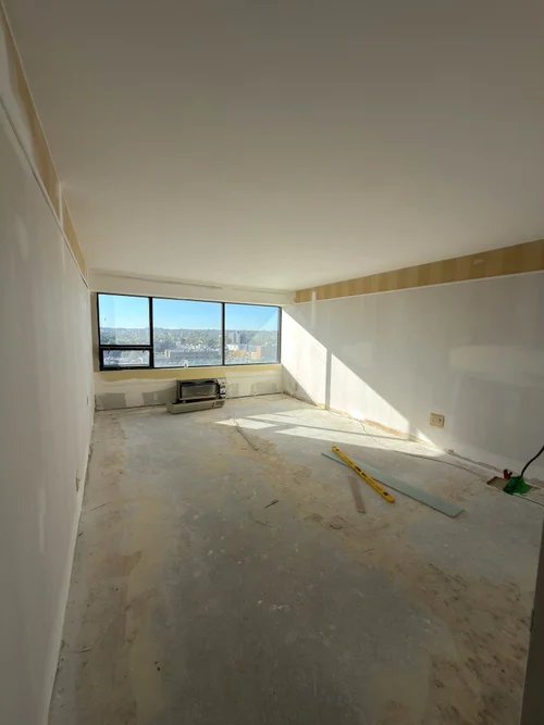 Unit during renovation, bare floor and drywall beside a wide window