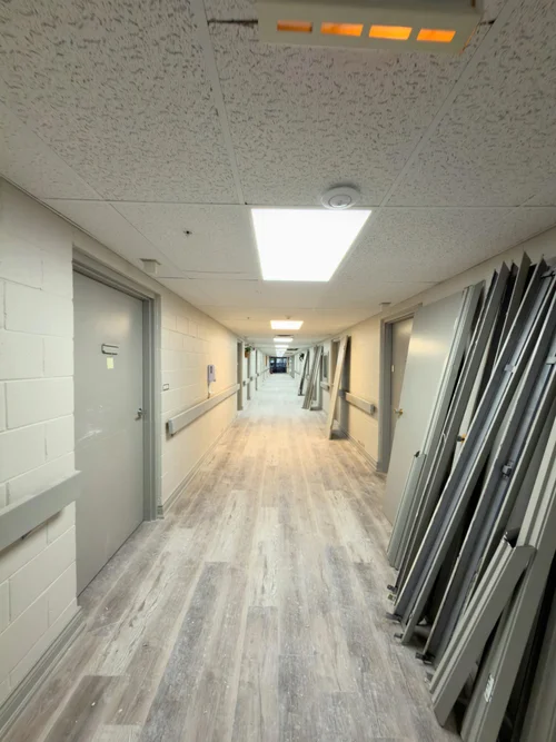 Corridor with new wood-look plank flooring and stacked door frames along the wall