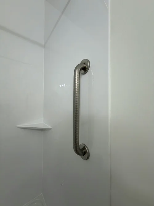 Brushed metal grab bar on a white shower wall beside a corner shelf