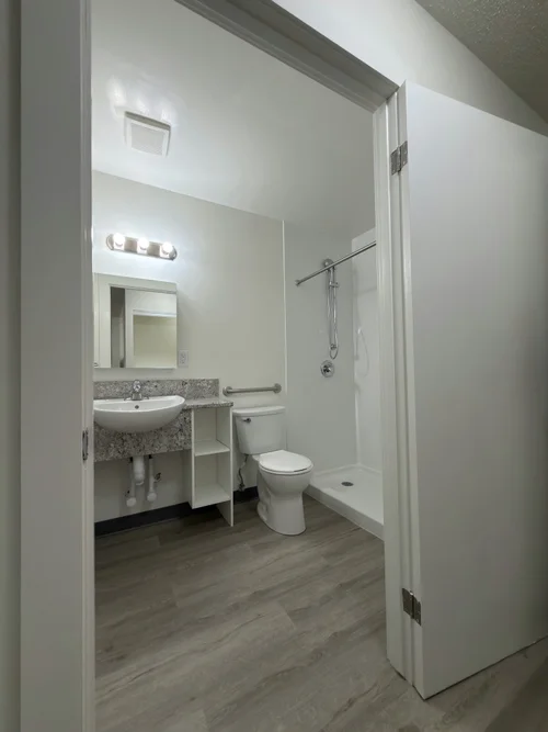 Accessible bathroom seen through a doorway, with wall-hung sink, toilet and roll-in shower