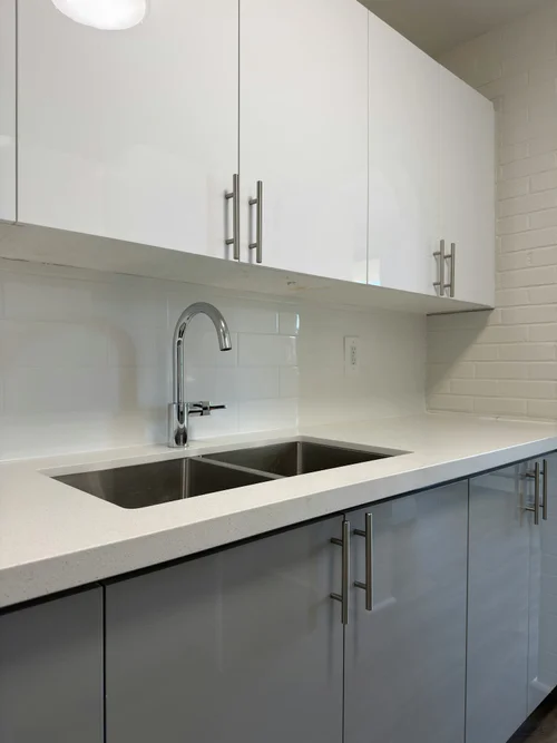 Double stainless sink with chrome faucet under white upper cabinets