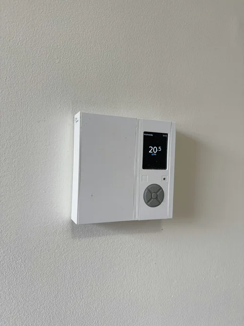 Digital thermostat with lit display mounted on a painted wall