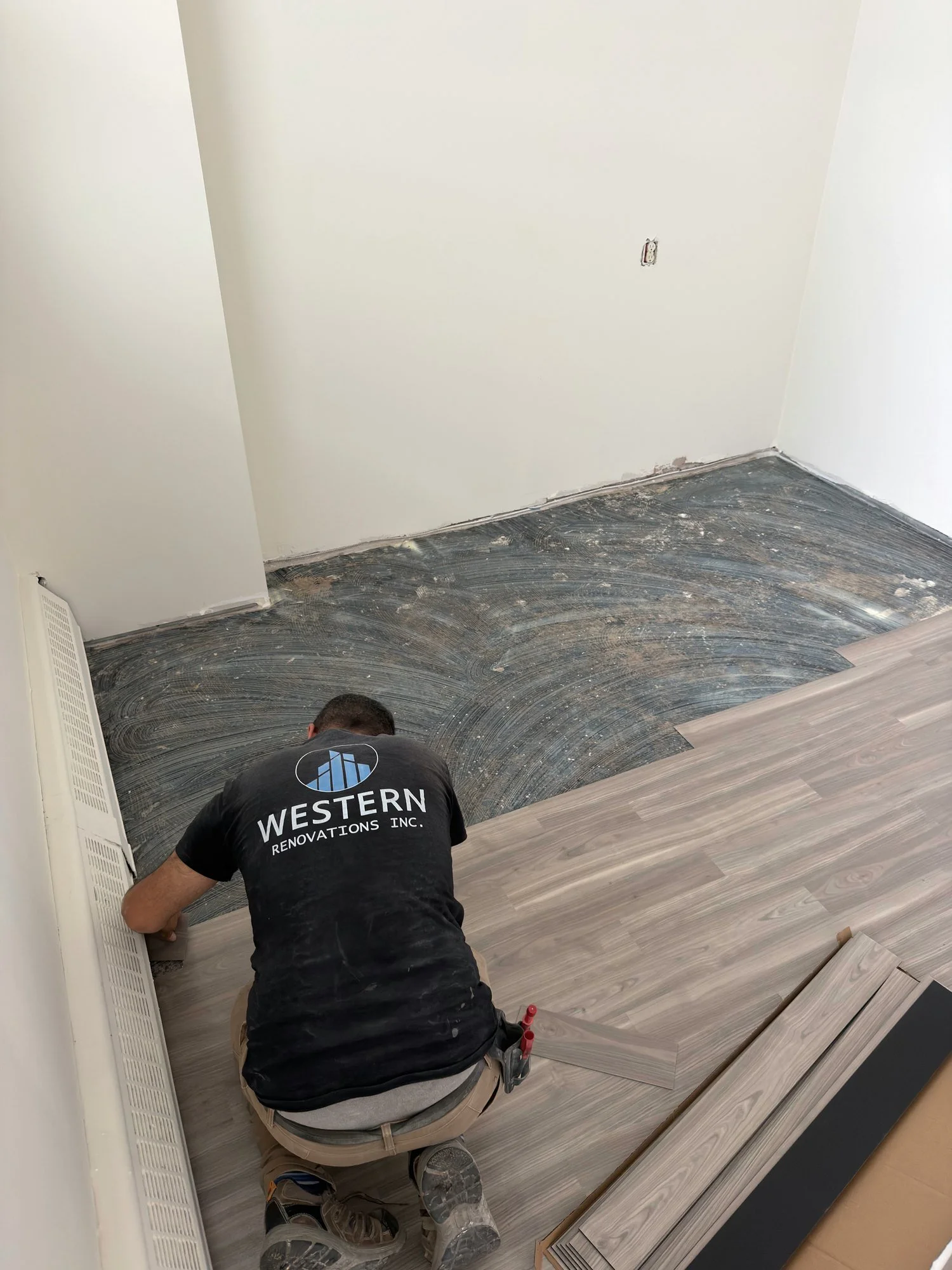 Installer kneeling to lay vinyl plank flooring in an empty room with white walls