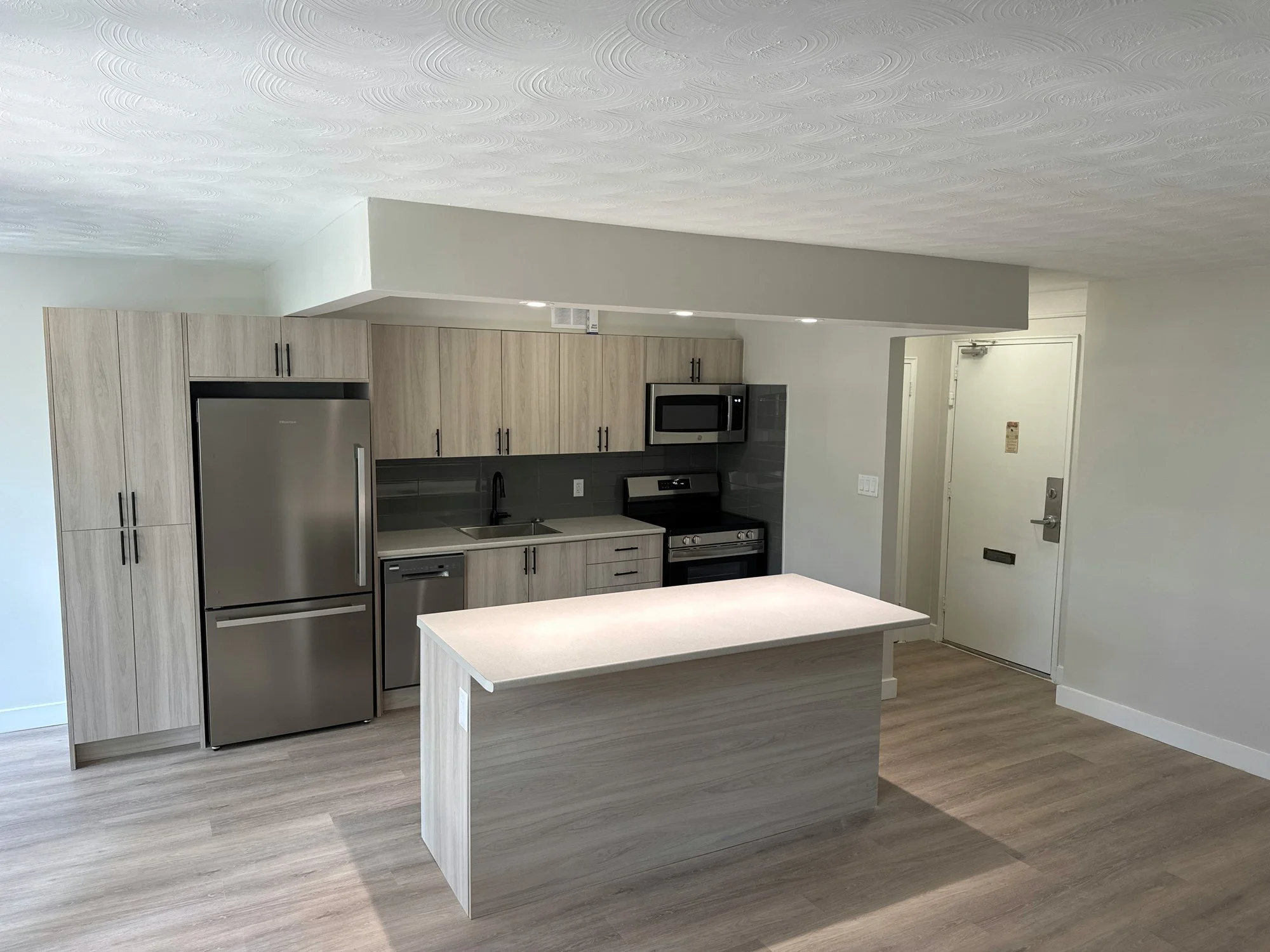 Renovated open kitchen with a centre island, stainless fridge and wood-look cabinets