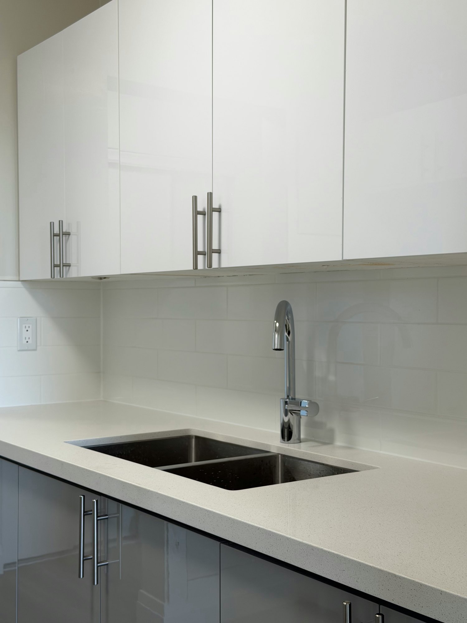 Finished kitchen with a double sink in a light counter, white gloss cabinets and a tile backsplash