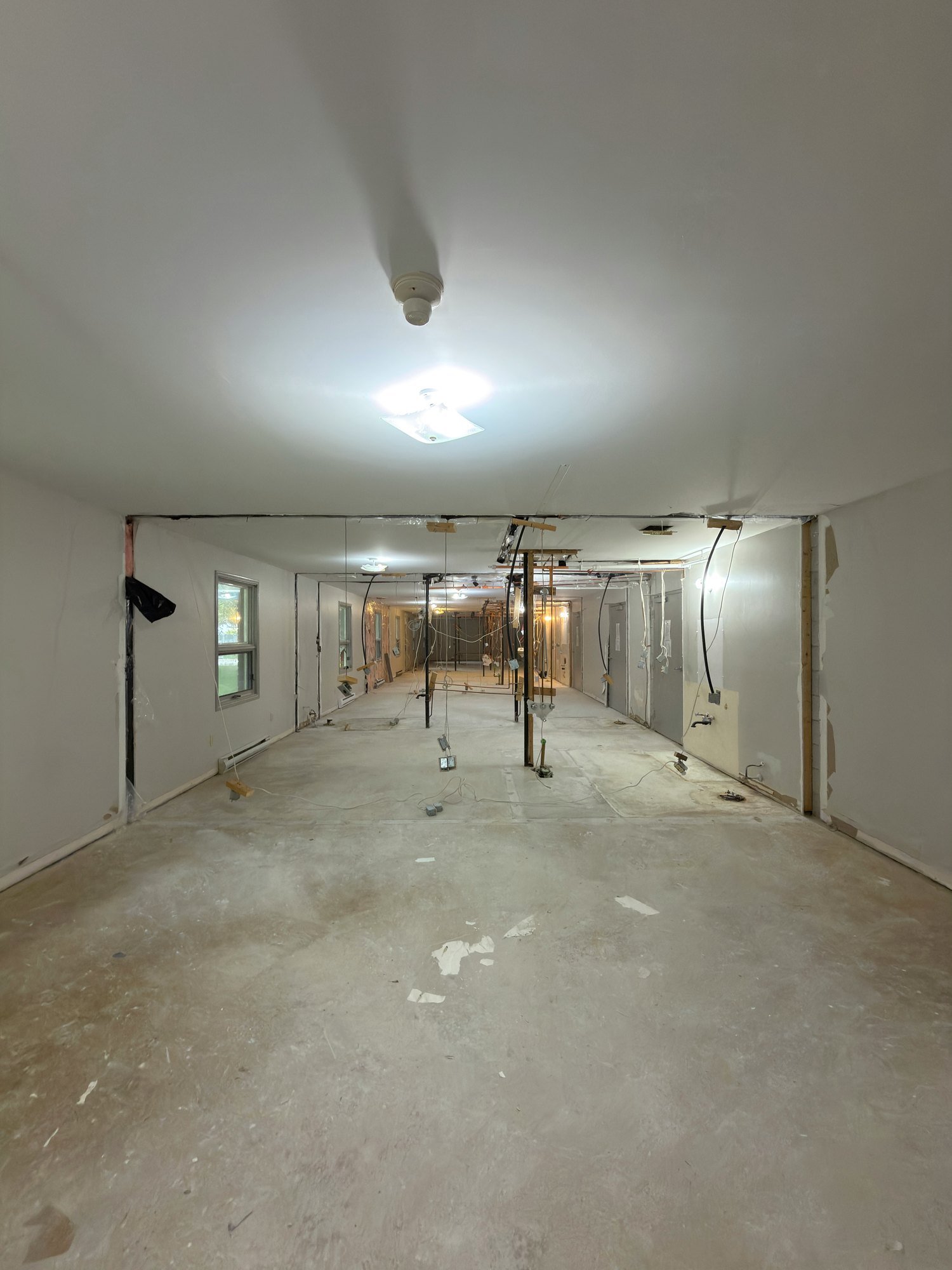 Long empty unit with flooring removed to bare concrete, exposed wires and a window along one wall