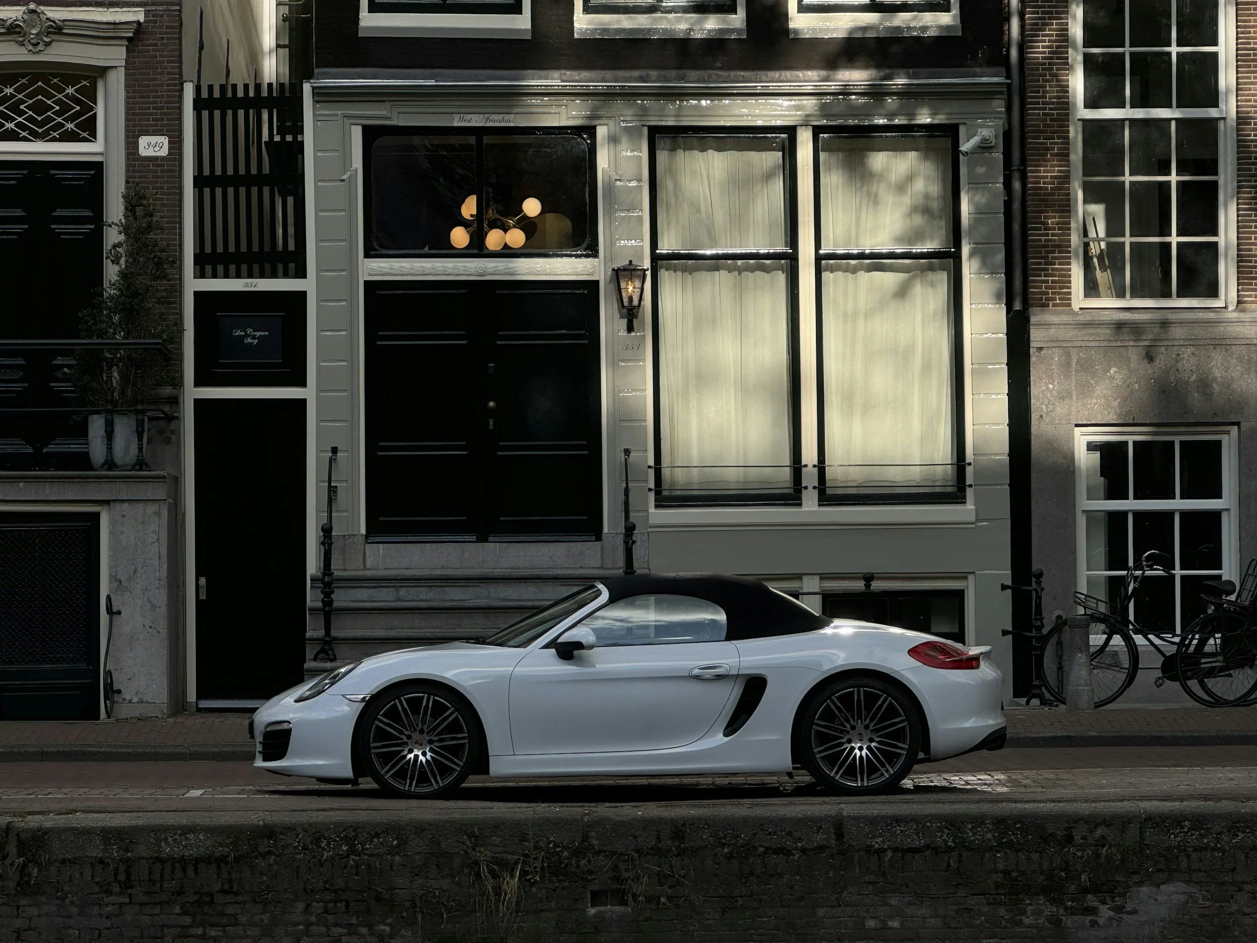 A white sports car with a black convertible top parked in front of a building on a city street.