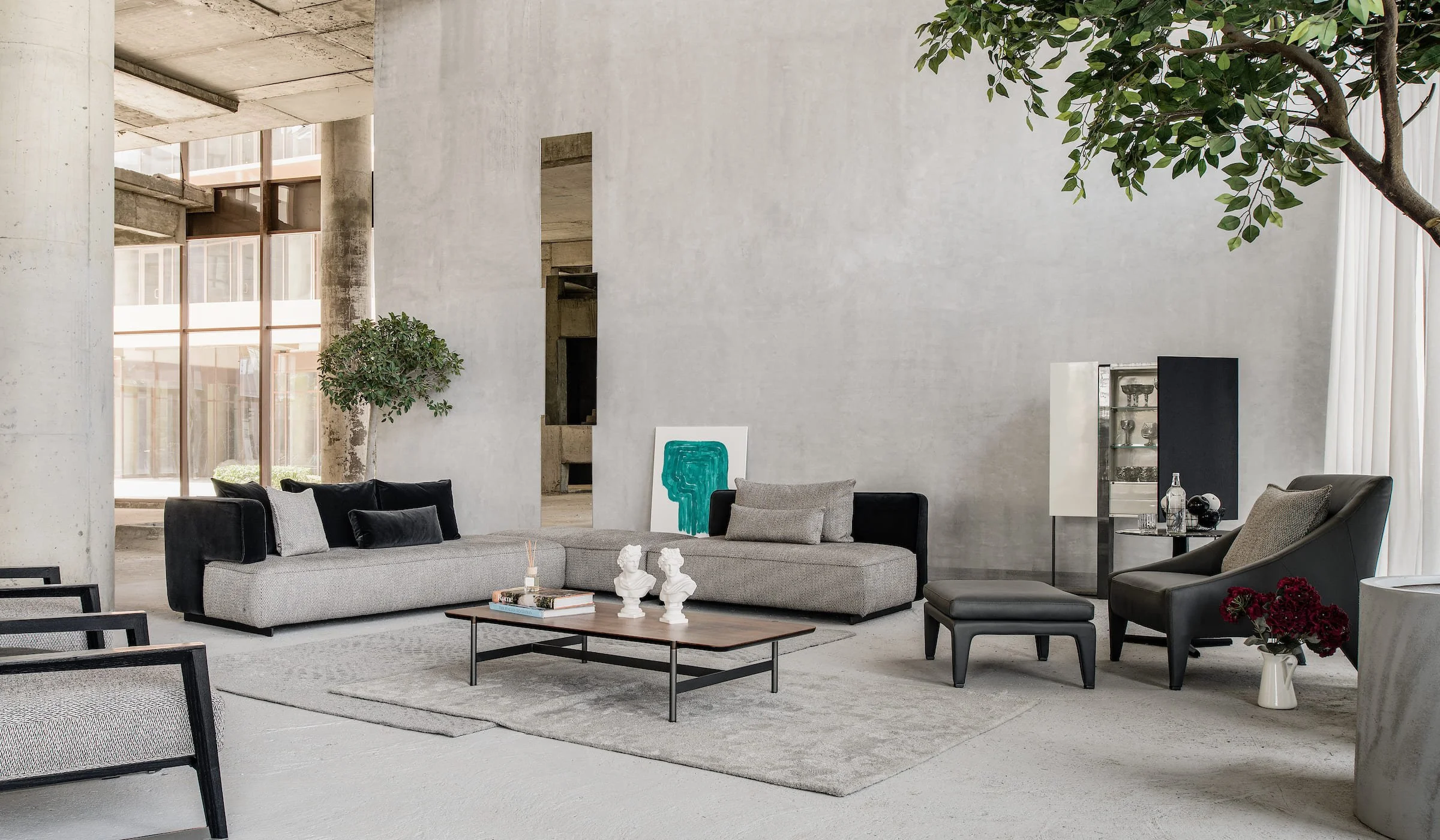 Modern living room with black and gray furniture, a coffee table, decorative busts, and large windows.