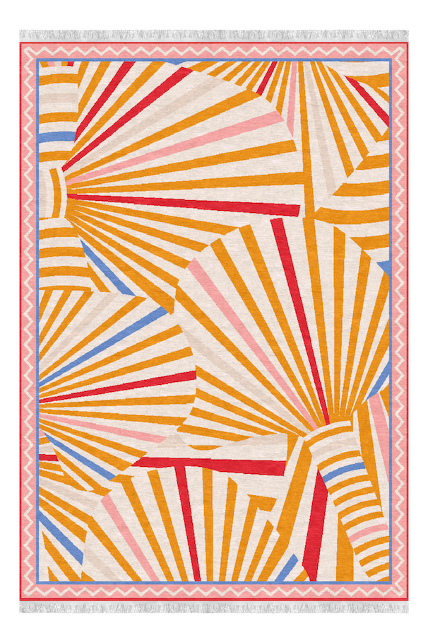 Colorful abstract geometric rug with fan-like patterns in shades of orange, red, pink, blue, and cream, bordered by a pink zigzag and cream stripe border, set on a gray floor.