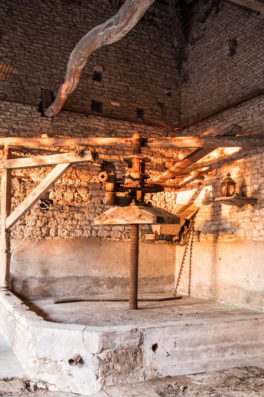An old, rustic wine press with a wooden screw and lever, set in a brick and stone cellar with warm lighting.