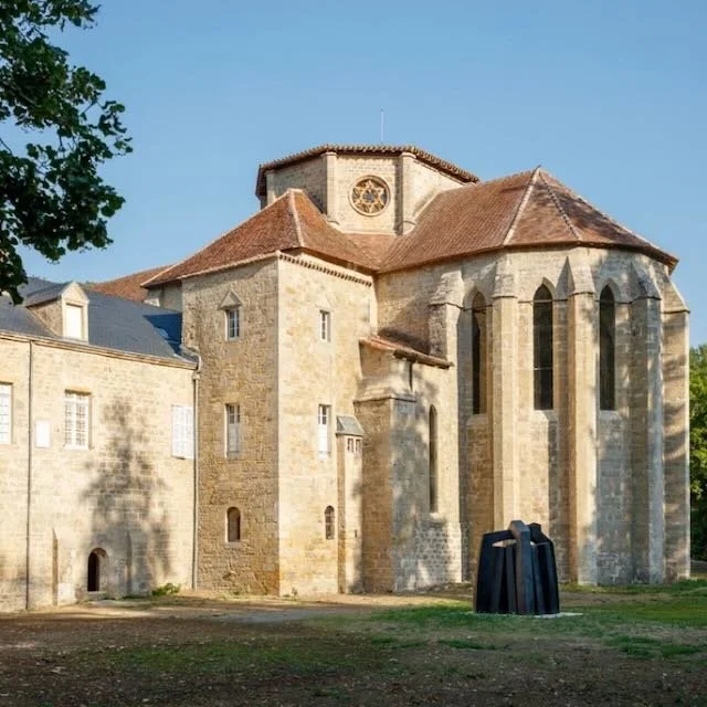 A historic stone church with arched windows and a round stained glass window near the roof, under a clear blue sky.