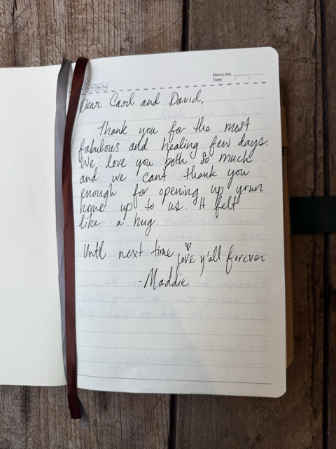 Open notebook with handwritten thank you note on lined paper, tied with a brown ribbon, placed on a wooden surface.