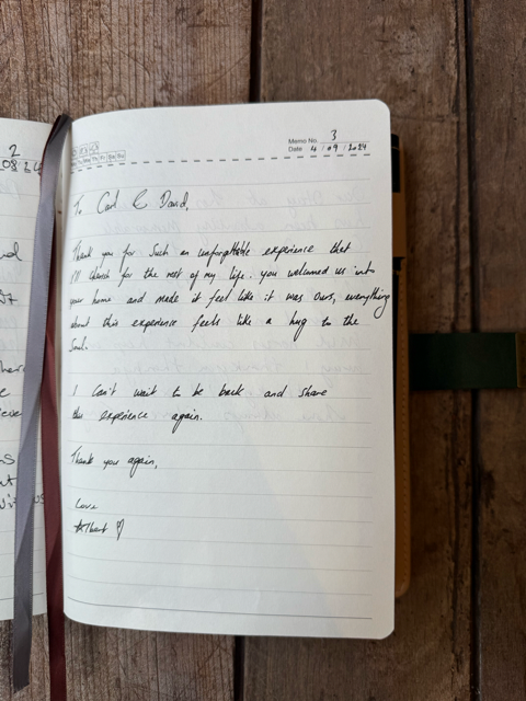 Open notebook with handwritten note on lined pages, attached to a red pen, on a rustic wooden surface.
