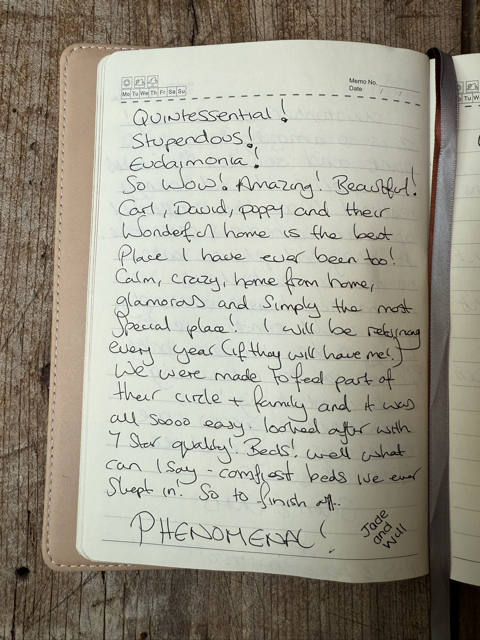 Open notebook with handwritten notes on pages, placed on a wooden surface. The notes express excitement and gratitude for a home, mentioning family, a circle, and a bed.
