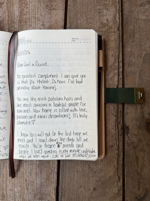 Open journal with handwritten message on a wooden table, secured with a green bookmark.