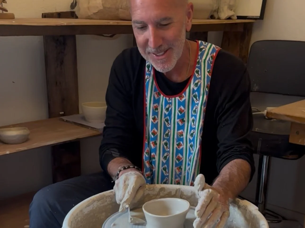 Man smiling while working with pottery on a wheel in a studio.