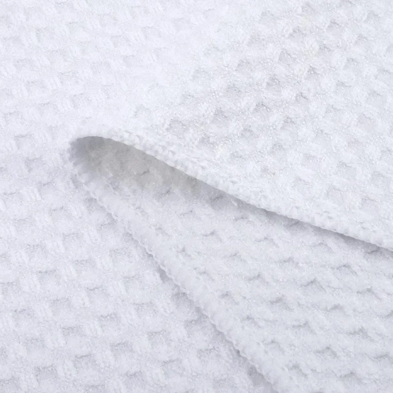 Close-up of a white waffle weave microfiber kitchen towel, highlighting its soft, absorbent texture and grid-like pattern, perfect for everyday kitchen use