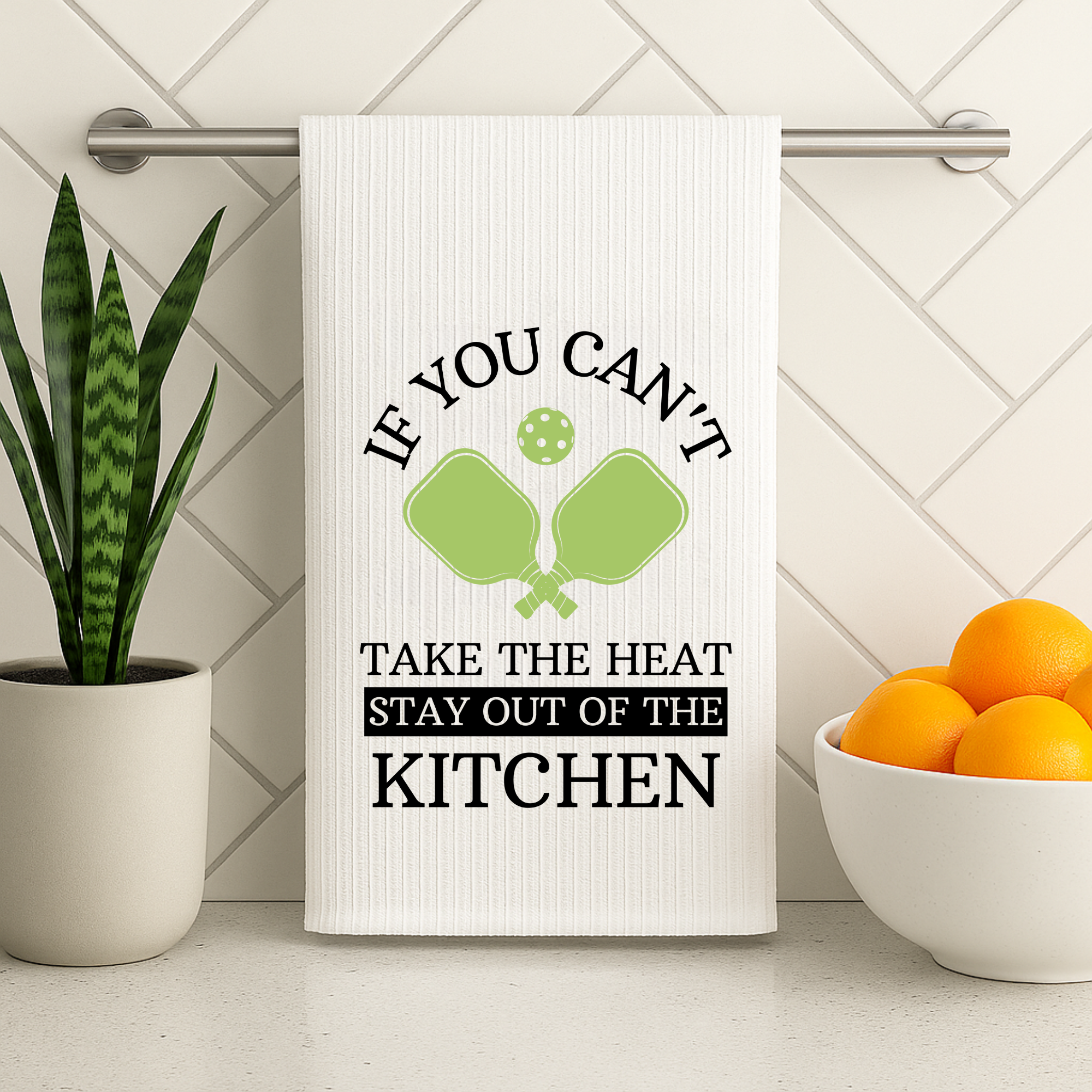 Pickleball kitchen towel hanging on a modern metal rod with oranges and a snake plant nearby.