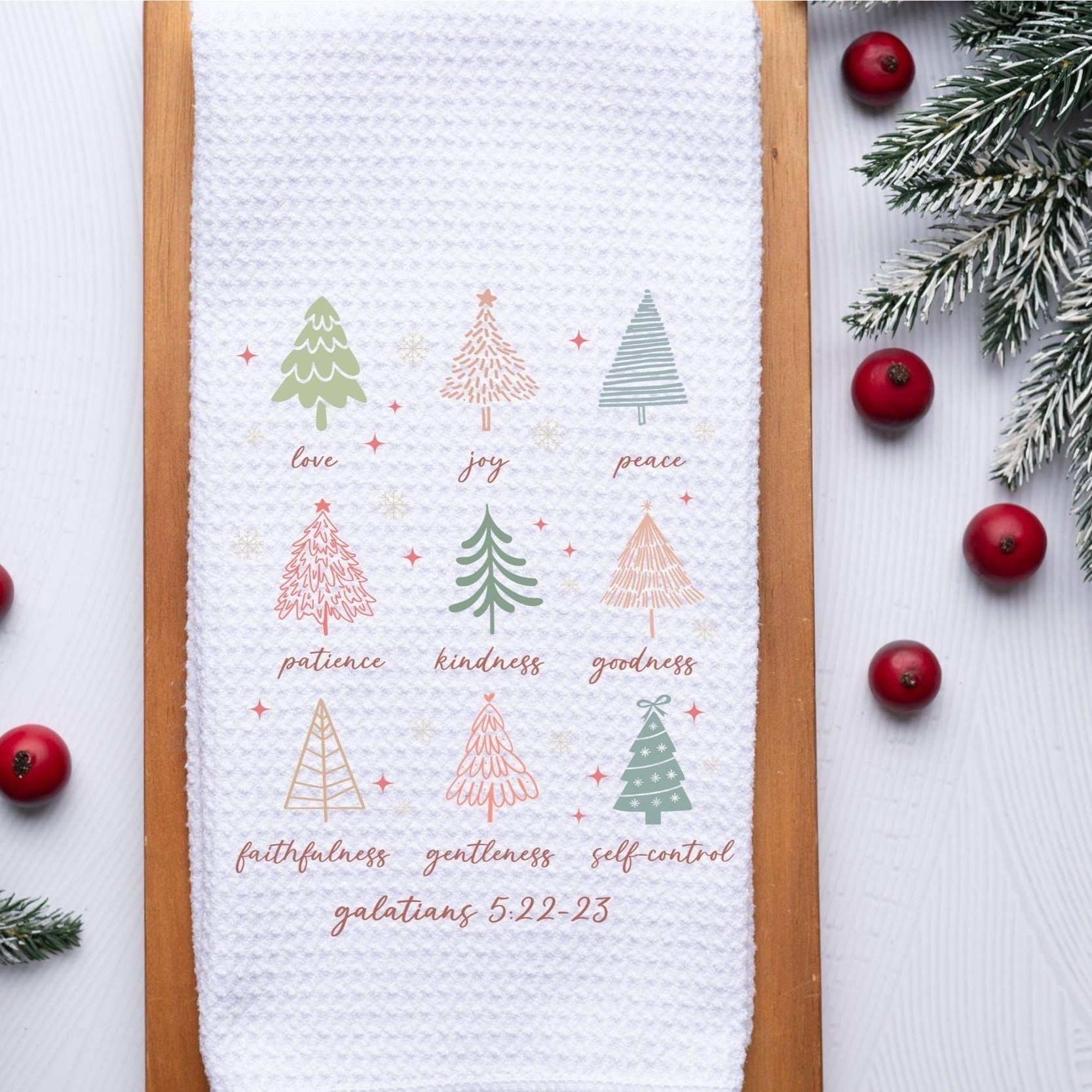 Galatians 5:22-23 holiday towel featuring fruits of the spirit and pastel Christmas trees, styled on wood tray with berries and greenery.