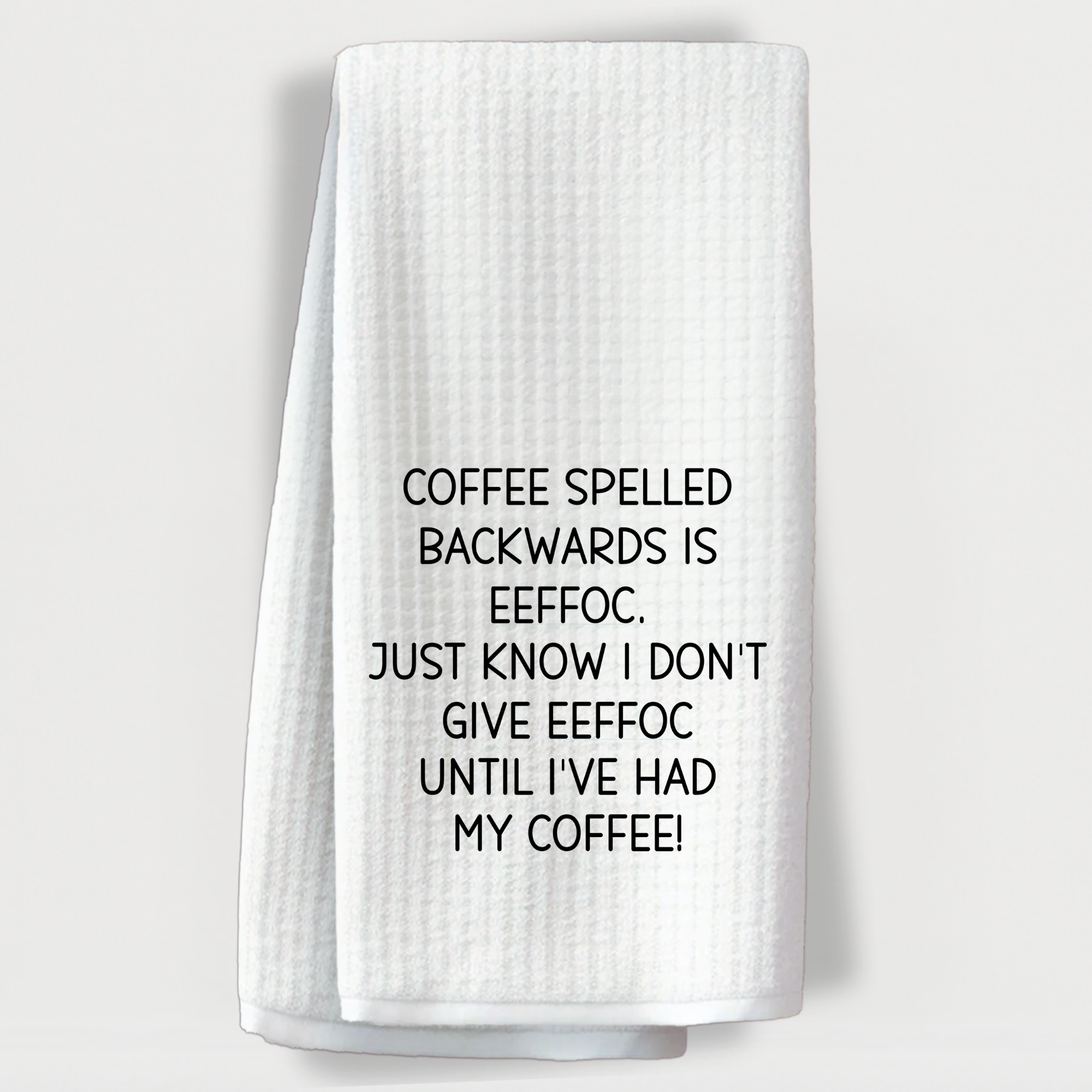 "Humorous coffee-themed towel with the quote 'Coffee spelled backwards is eeffoc…' in black text."
