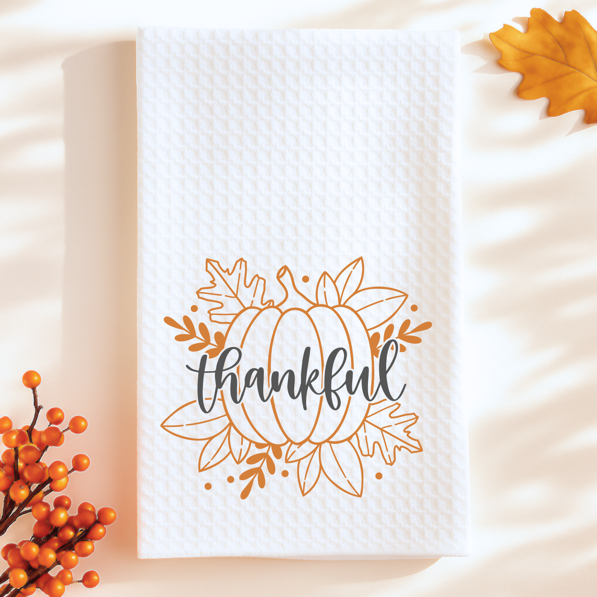 White waffle weave kitchen towel with pumpkin and thankful text, styled with fall leaves.