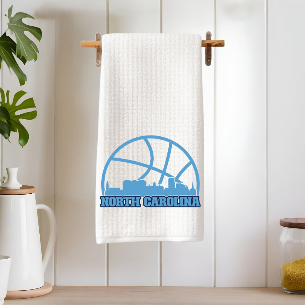 North Carolina basketball-themed dish towel hanging on wood rod in clean white kitchen.