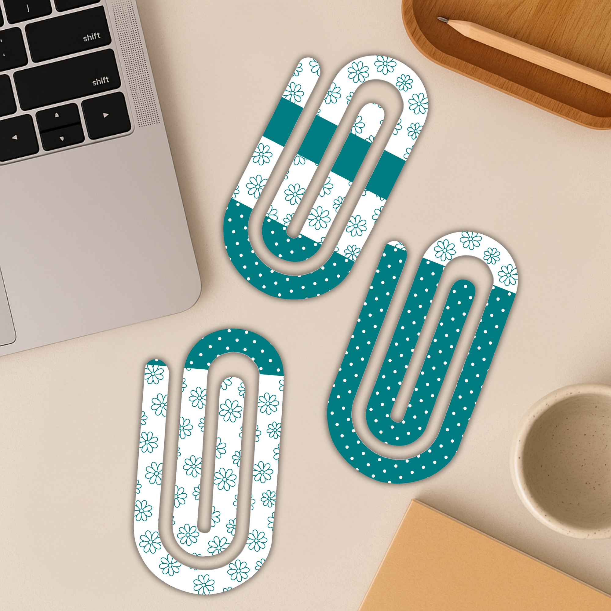 Three jumbo acrylic paperclips in floral and stripe designs placed on a workspace beside a laptop.