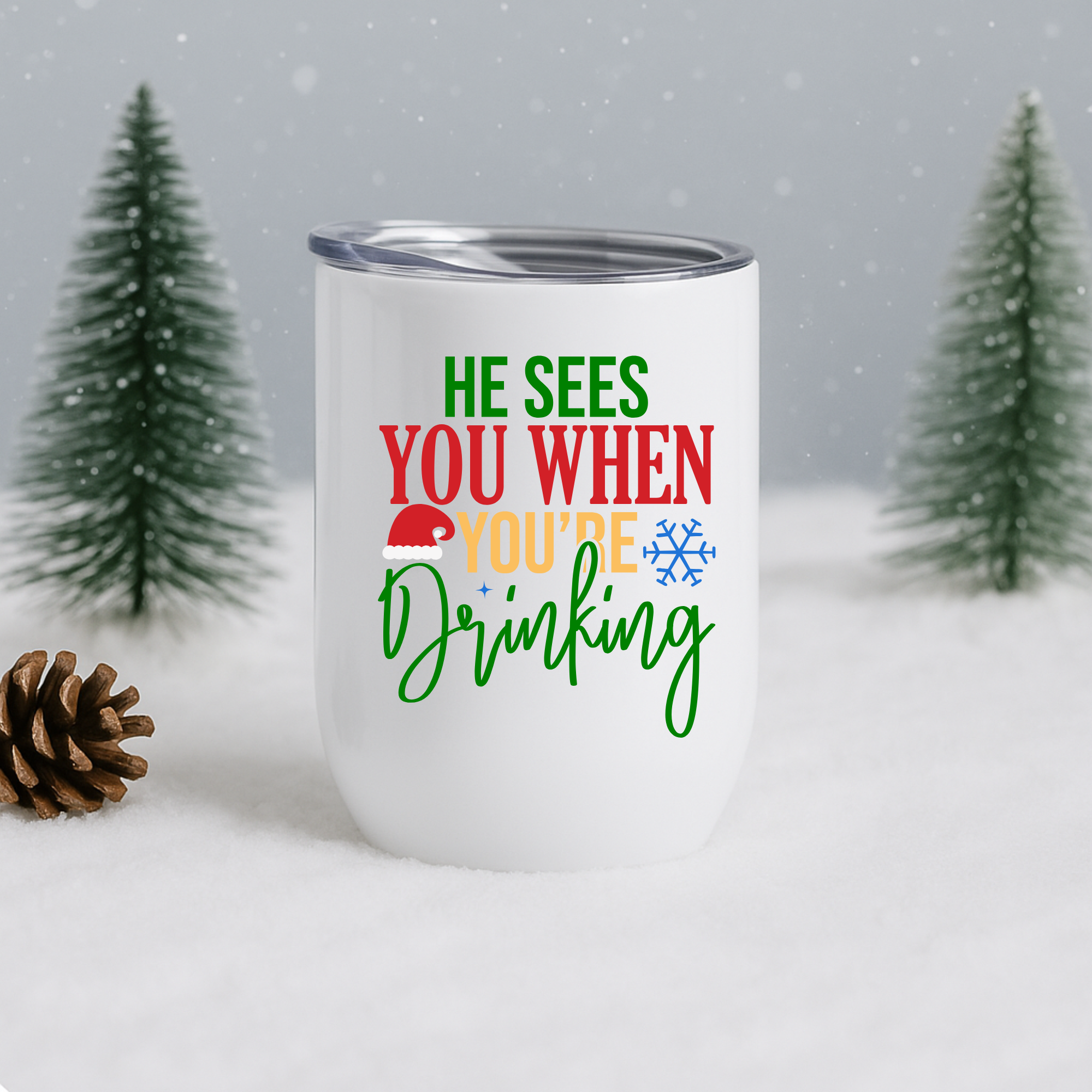 White stainless steel holiday tumbler with “He Sees You When You’re Drinking” design shown in snowy pine winter background.