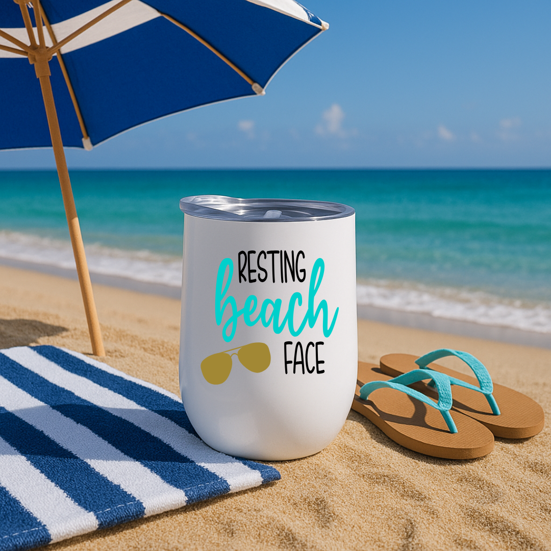 White wine tumbler under umbrella on sandy beach with “Resting Beach Face” design in turquoise and sunglasses graphic.