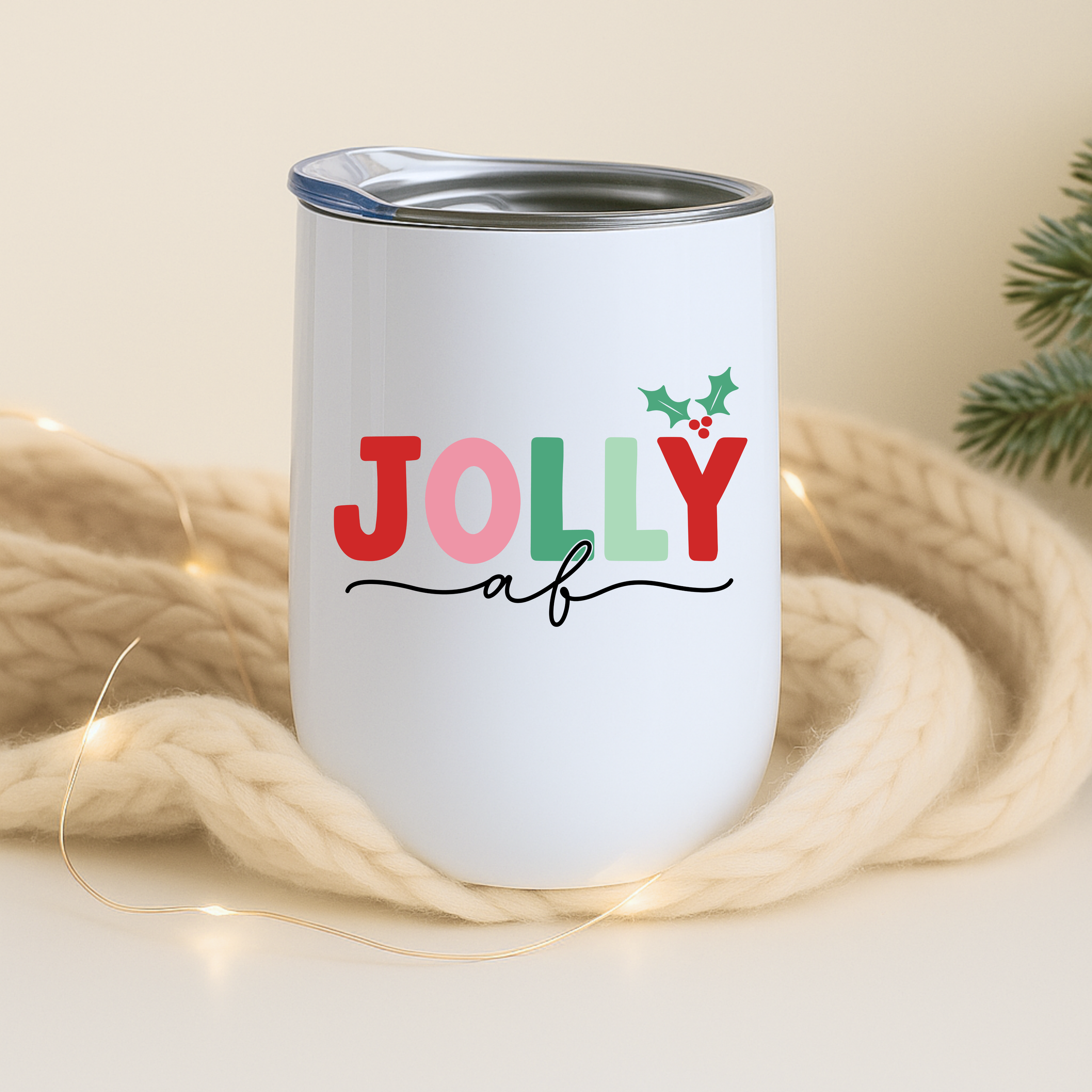 Jolly AF tumbler resting on a soft knit blanket with warm string lights.