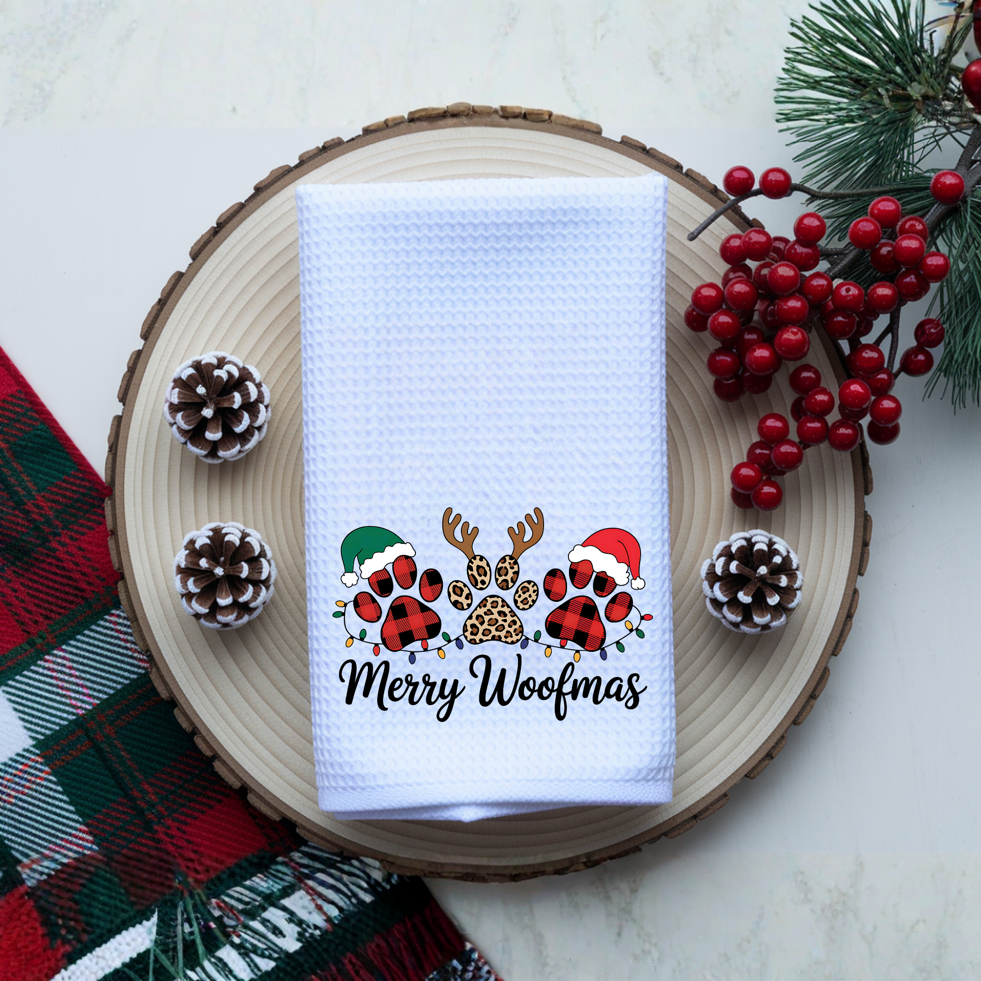 Merry Woofmas dog Christmas kitchen towel styled flat lay with pinecones and holiday greenery.