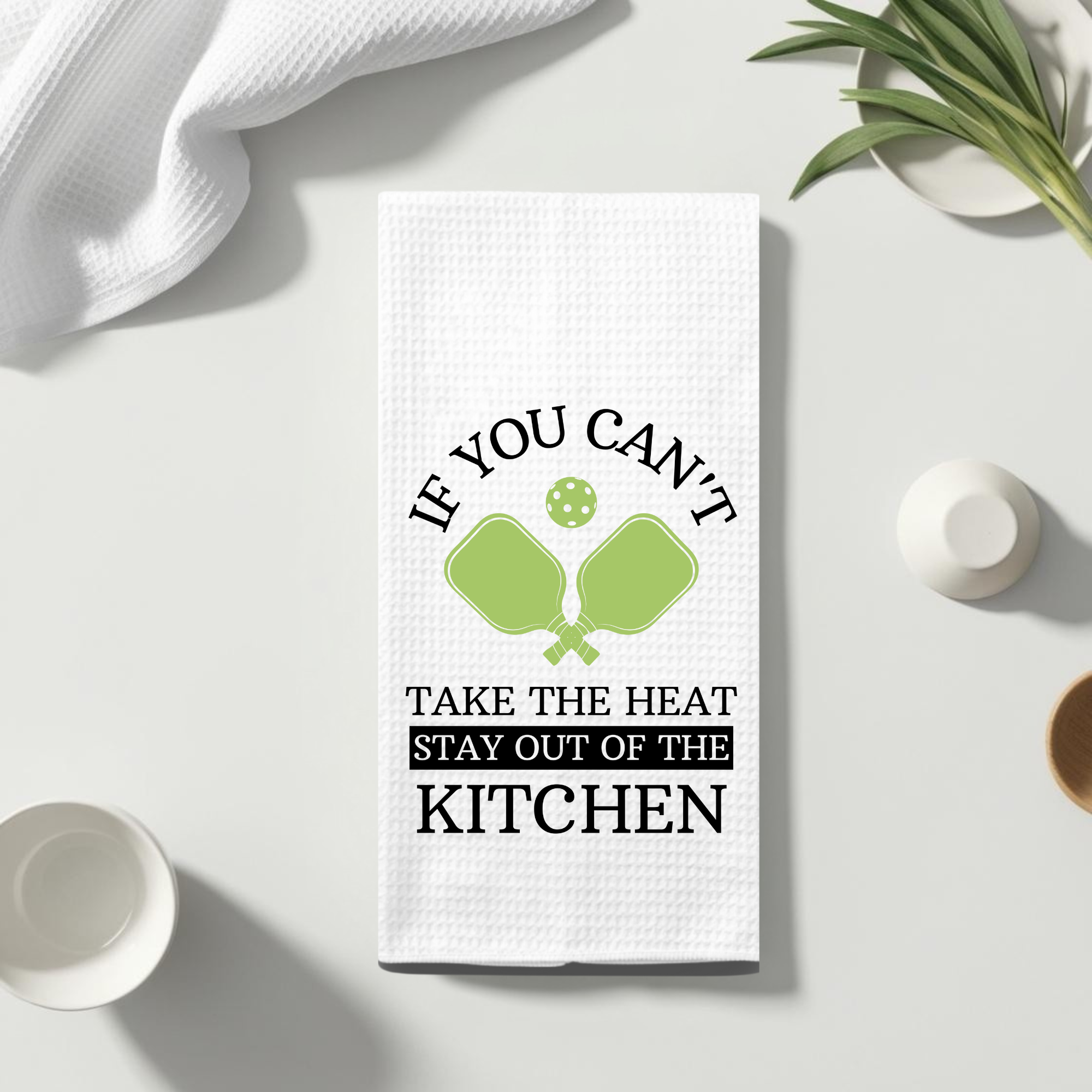 Waffle weave towel featuring pickleball design laid flat on a bright kitchen surface with plates and linens.