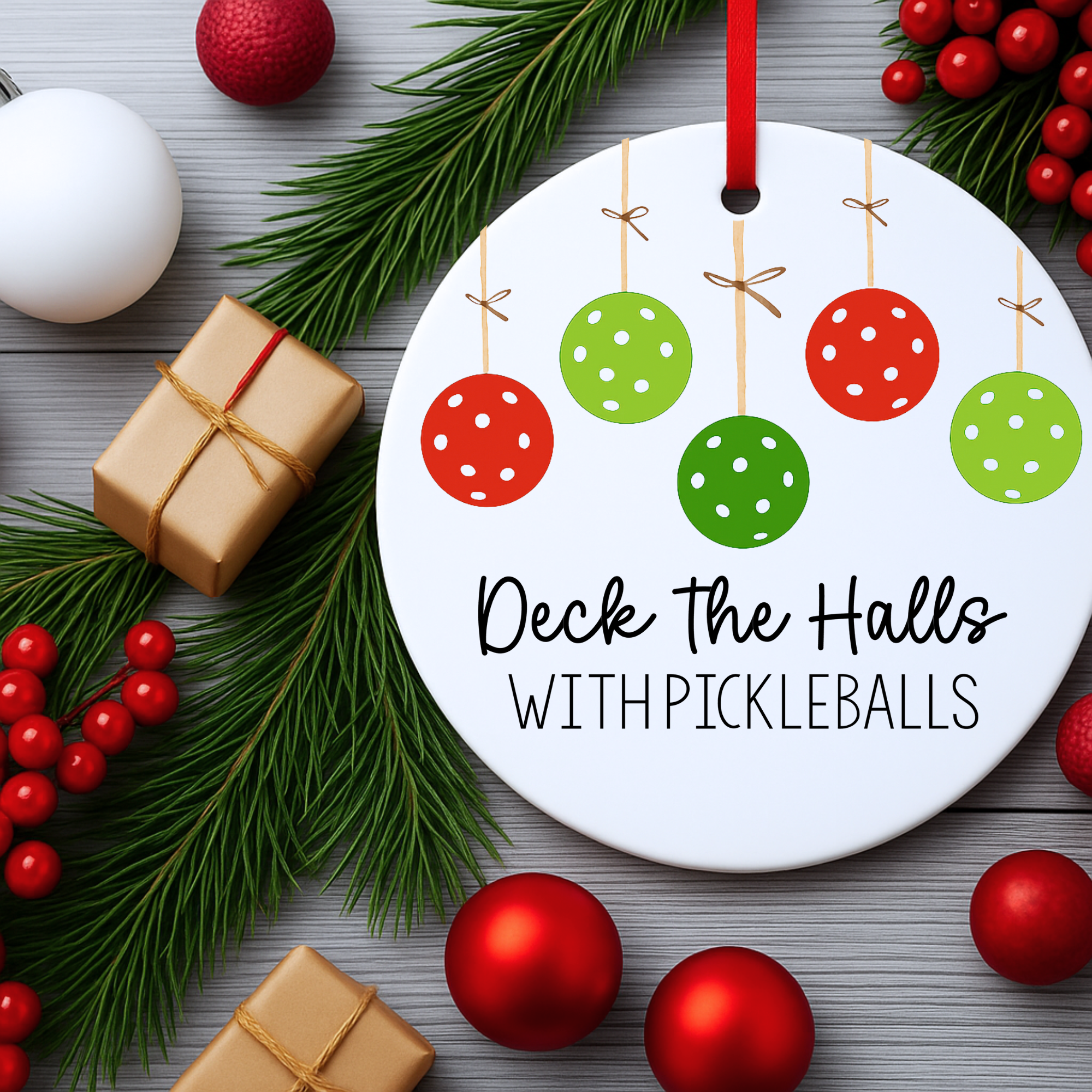 “Deck the Halls with Pickleballs ornament displayed with greenery, ornaments, and wrapped gifts.”
