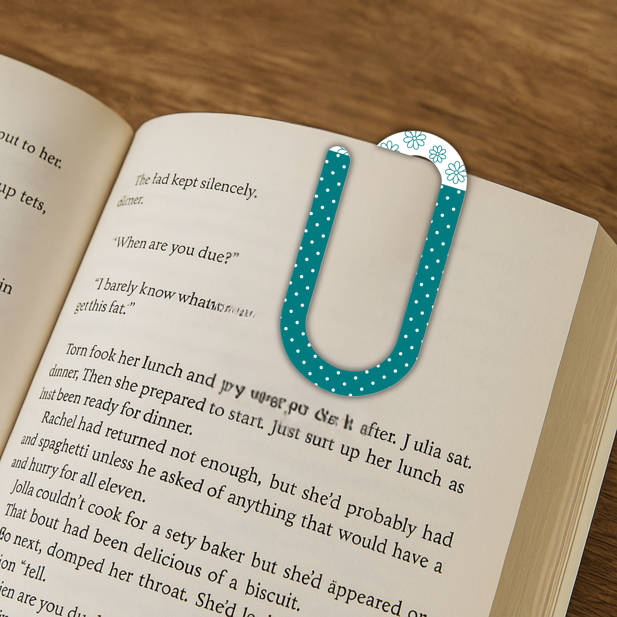 Jumbo polka dot acrylic paperclip used as a bookmark inside an open book on a wood table.