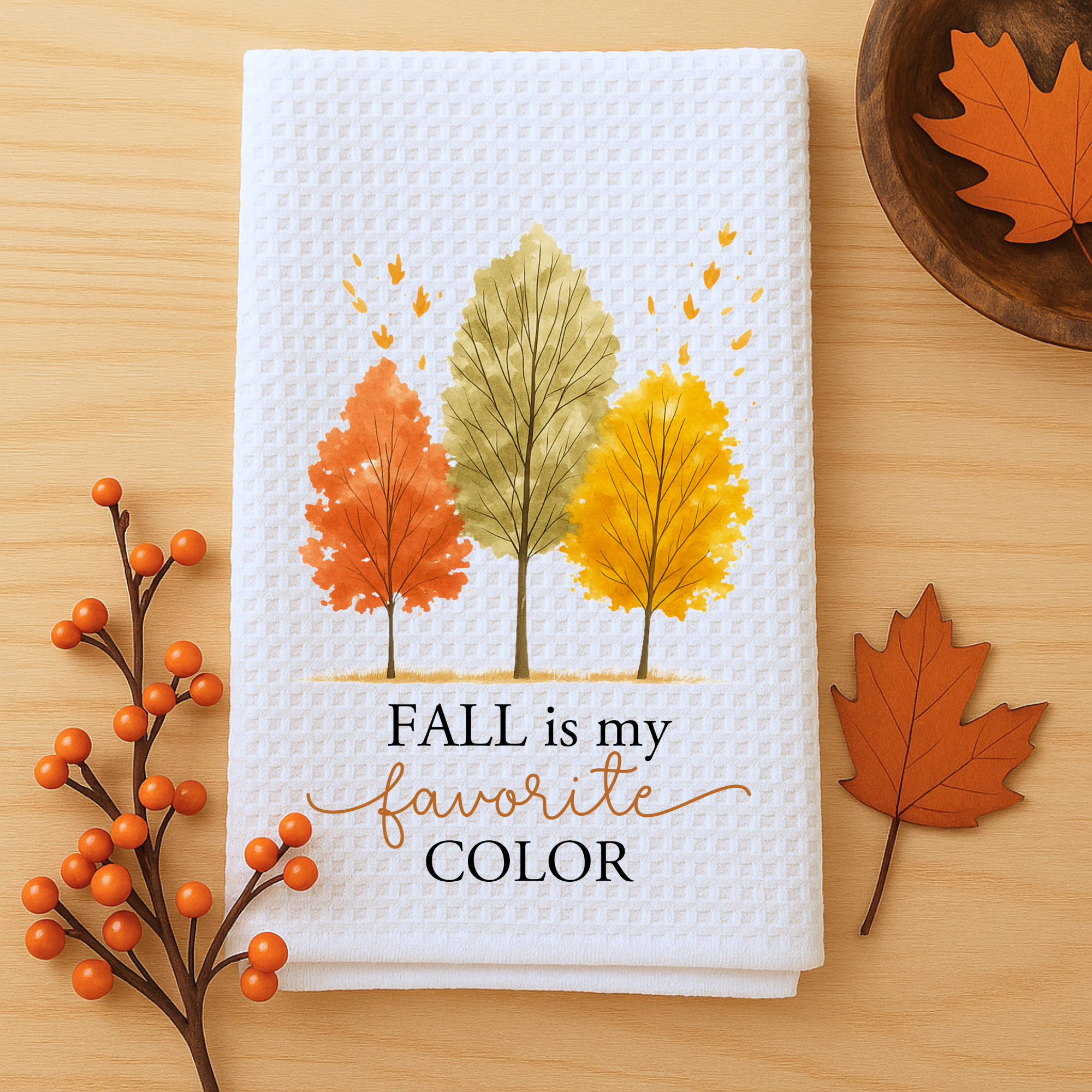 Fall decor kitchen towel featuring “Fall is My Favorite Color” quote styled flat with leaves and a wooden bowl.