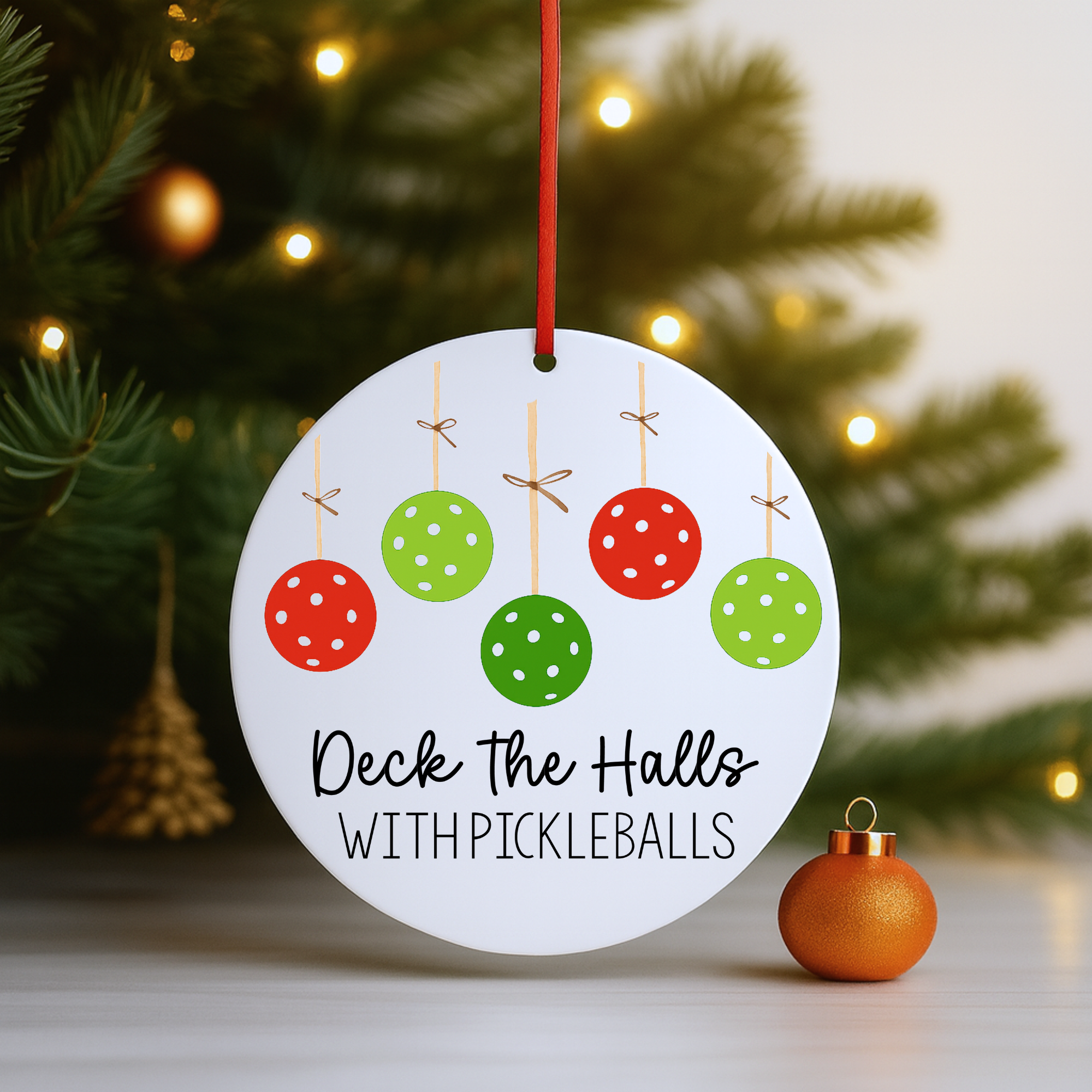 “Round Deck the Halls with Pickleballs ornament hanging on a Christmas tree with warm holiday lights.”
