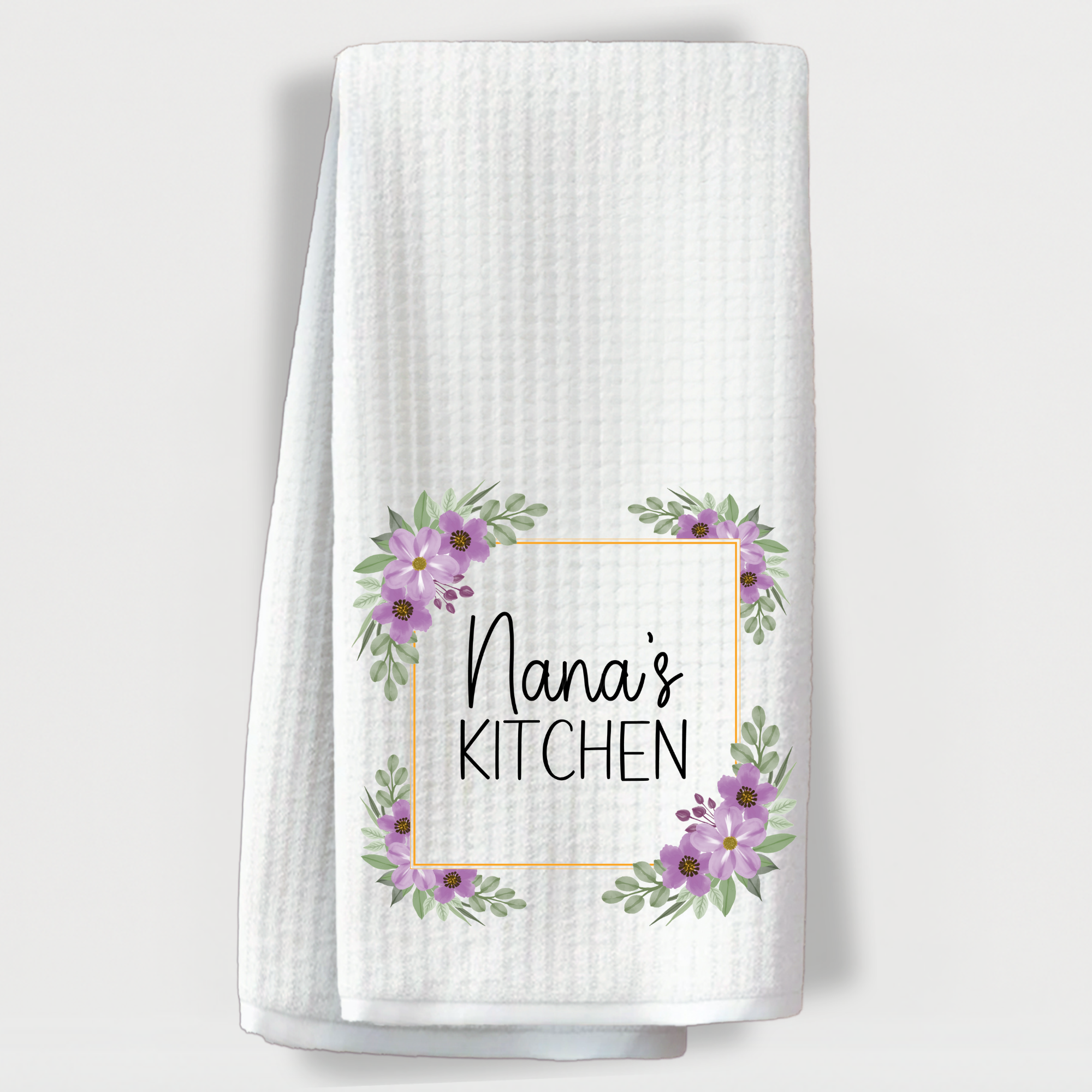 "White waffle towel with 'Nana’s Kitchen' text surrounded by purple floral accents in each corner."