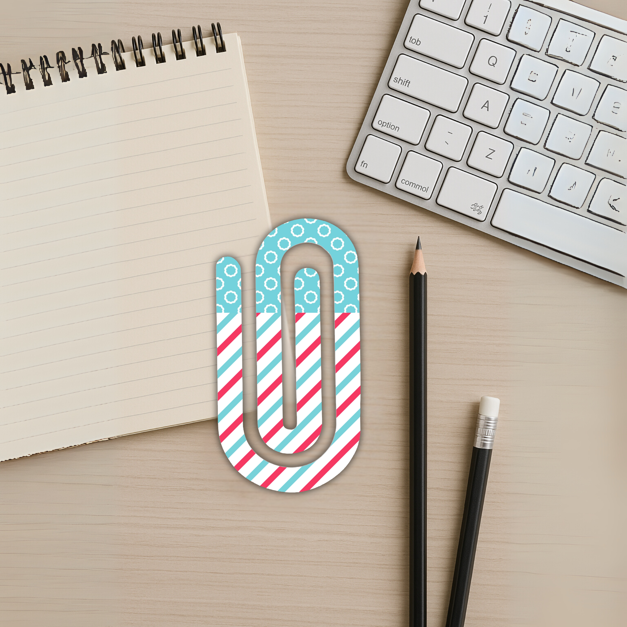 Cute jumbo paper clip styled on a desk with keyboard and notepad.