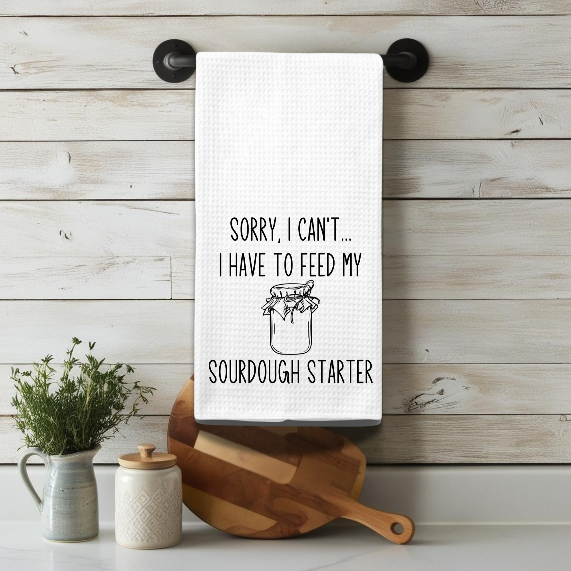 Waffle weave kitchen towel hanging on rustic white backsplash – sourdough humor for home chefs.