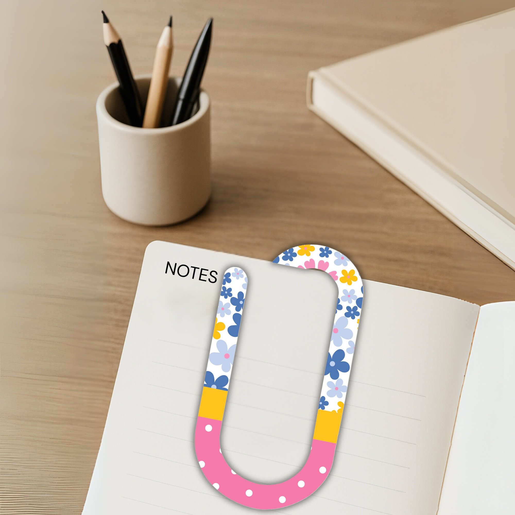 Decorative jumbo paper clip attached to note page with pencil cup in background.
