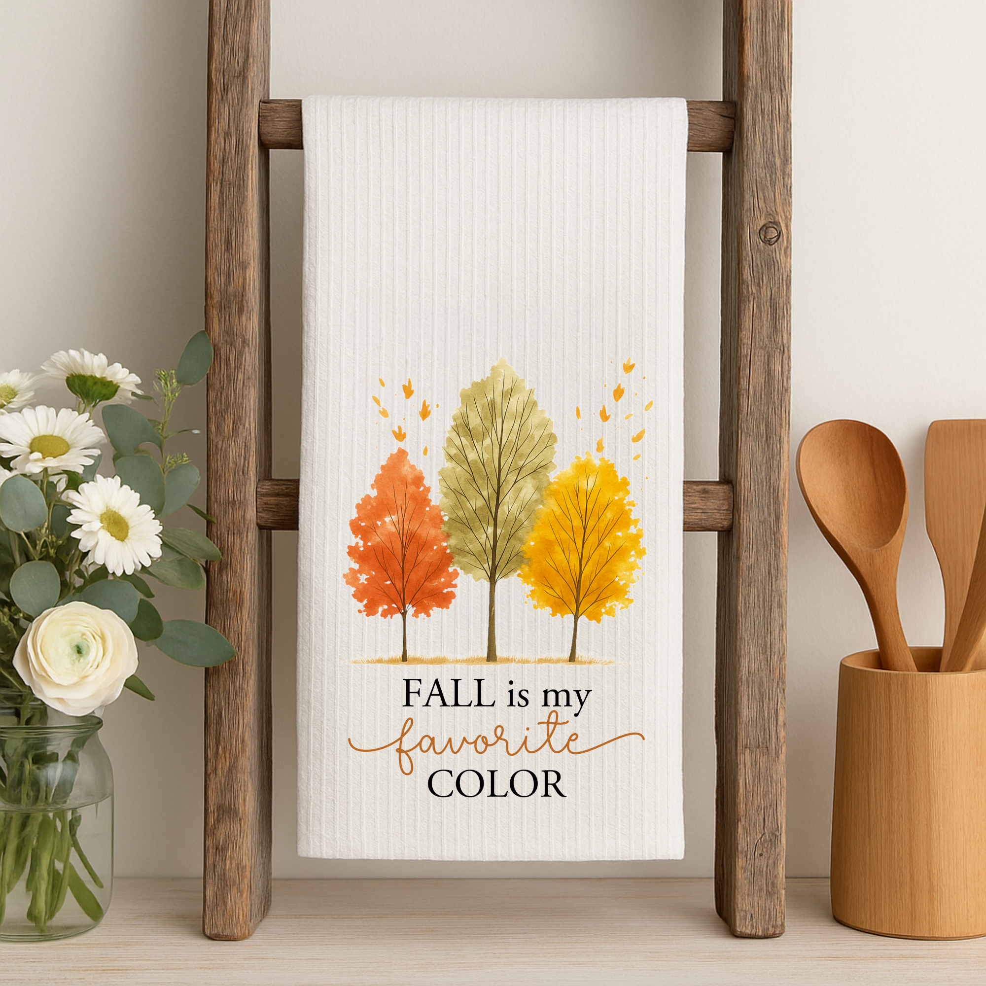 Fall themed dish towel with autumn tree design displayed on a rustic ladder with wooden utensils, farmhouse fall decor.